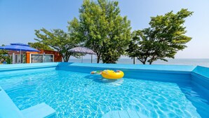 A clear blue swimming pool with a yellow inflatable ring, surrounded by trees and a building with a blue roof. - Ganghwa Badatgashimteo Pension (Incheon)