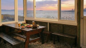 A wooden table with benches, a meal, and a view of a body of water at sunset. - Ganghwa Badatgashimteo Pension (Incheon)