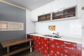 A kitchen with white upper cabinets, a red lower cabinet with floral patterns, a stainless steel sink, and a wooden bench. - Ganghwa Badatgashimteo Pension (Incheon)