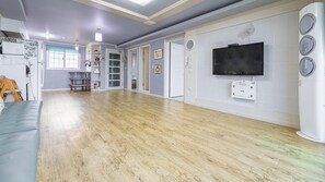 A spacious room with a wooden floor, a television mounted on the wall, and a white appliance on the right. - Ganghwa Badatgashimteo Pension (Incheon)