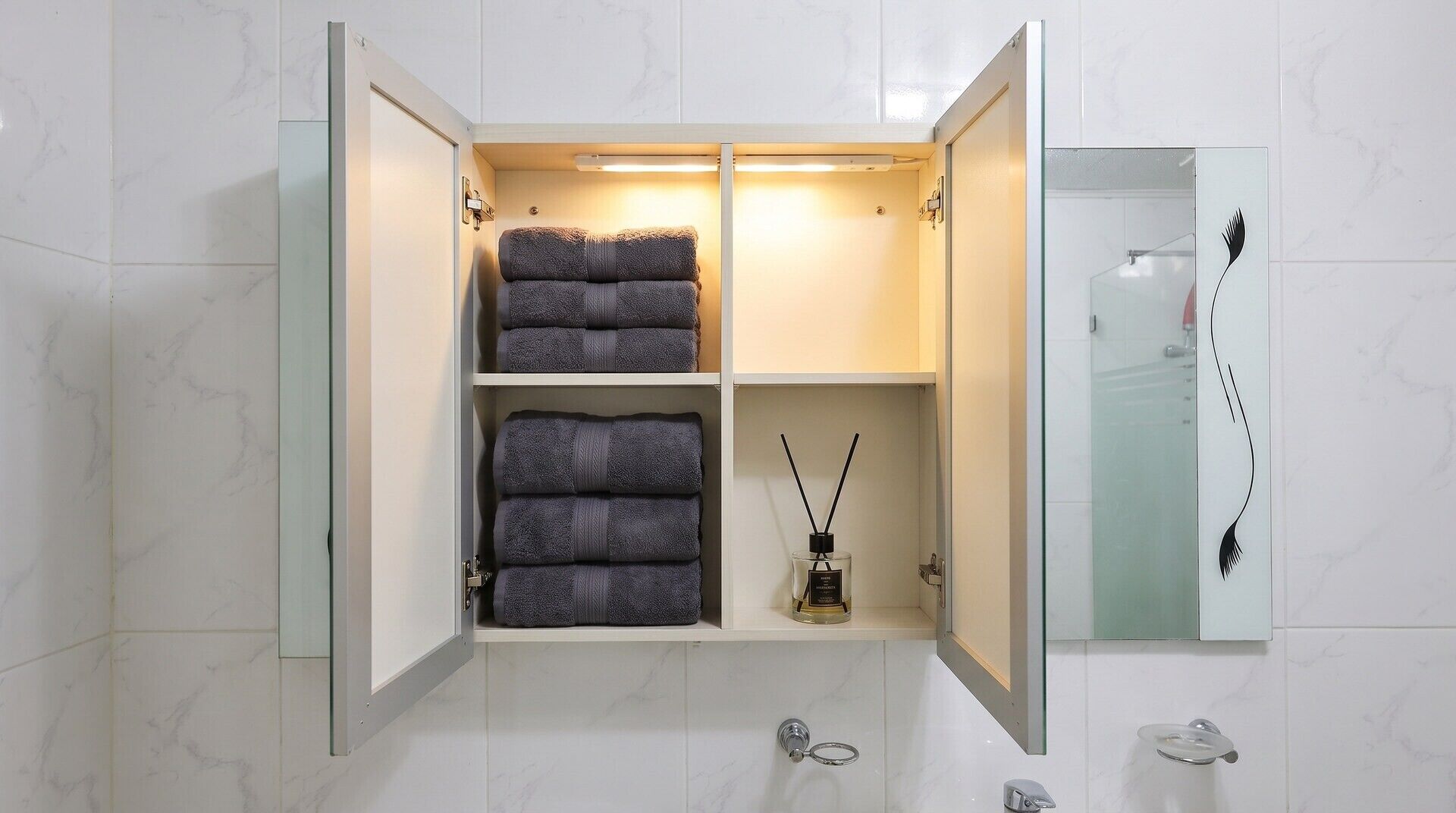 A bathroom with a glass-fronted cabinet containing folded towels and a bottle of reed diffuser.