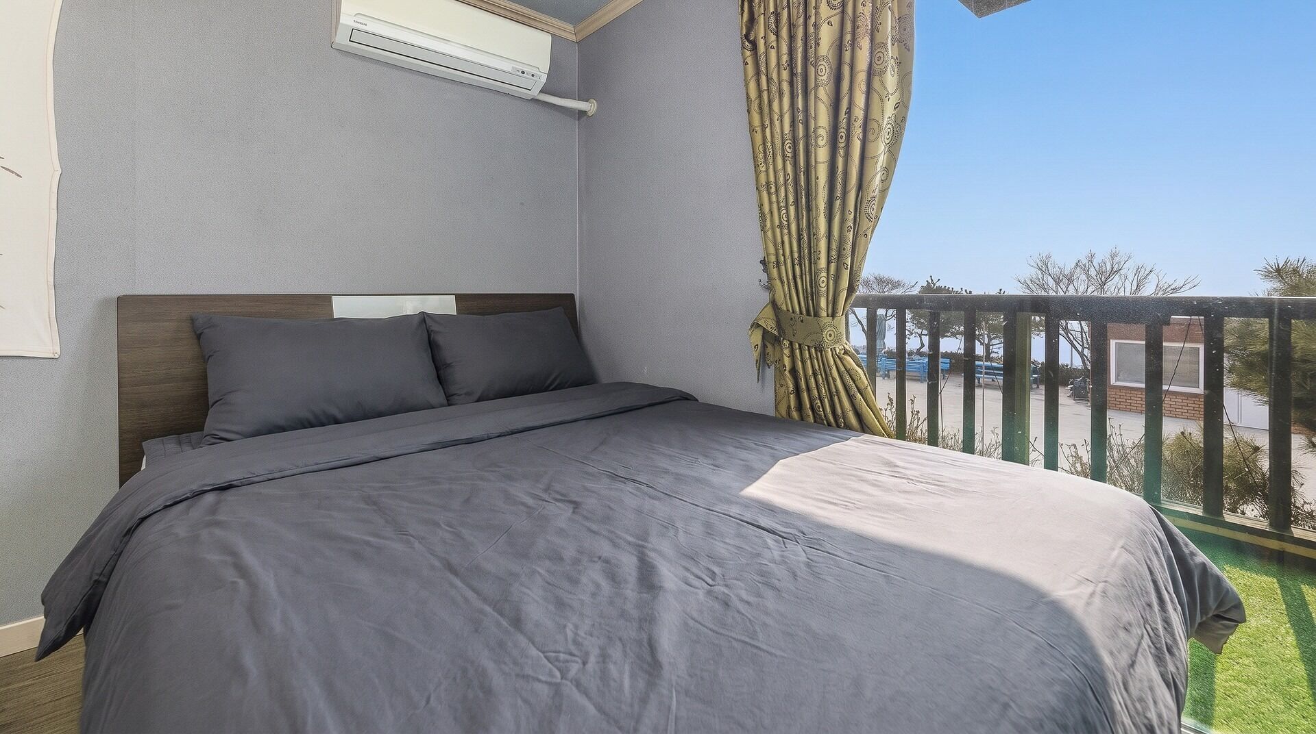A bedroom with a bed, grey bedding, a window, and a view of the outside.