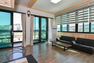 Uma sala de estar espaçosa com uma grande porta de vidro deslizante que dá para uma varanda, um sofá de couro preto, uma mesa de centro de madeira e um ar condicionado instalado.
