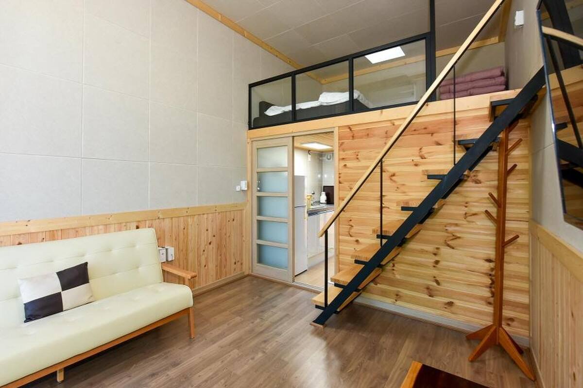 Una habitación con escalera de madera, un sofá y una puerta de cristal que da a una zona de cocina.