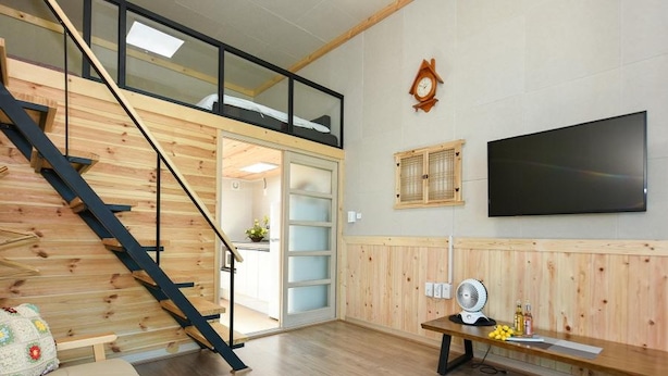 A modern interior with a wooden staircase, a flat-screen TV, and a bench with a fan.