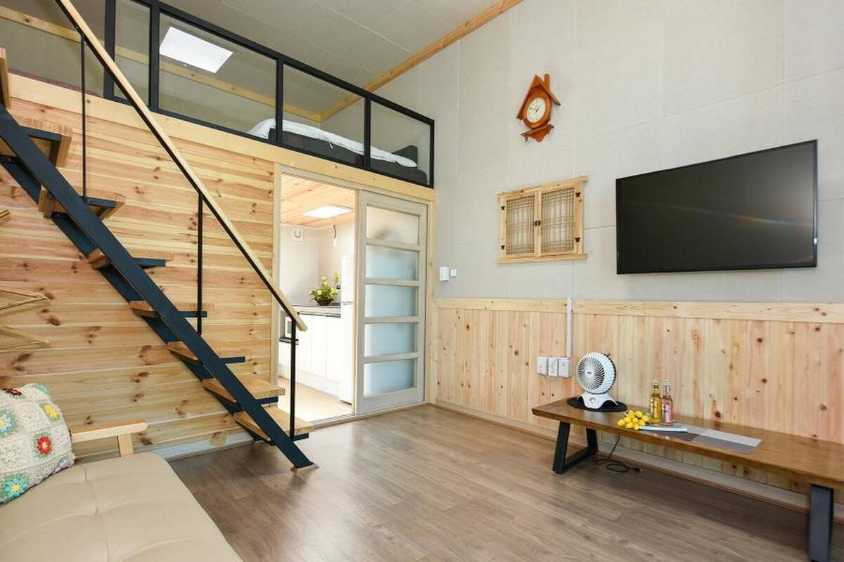 Un interior moderno con una escalera de madera, un televisor de pantalla plana y un banco con un ventilador.