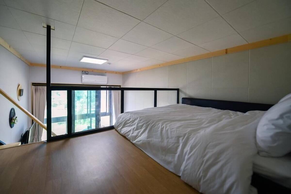 Un dormitorio con cama, ventana, piso de madera y luz en el techo.
