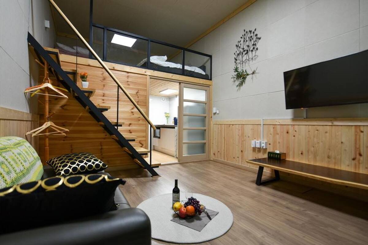 Una sala de estar moderna con una escalera de madera, un televisor de pantalla plana y una mesa redonda con fruta.