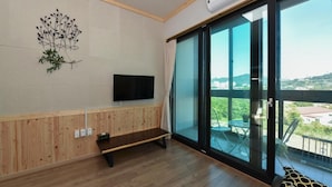 A modern room with a large sliding glass door leading to an outdoor balcony, a flat-screen TV mounted on the wall, and a wooden bench.