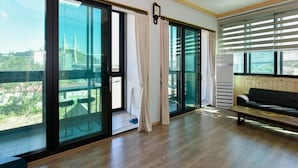 A spacious living area with large sliding glass doors leading to a balcony, a black sofa, and a wooden bench.