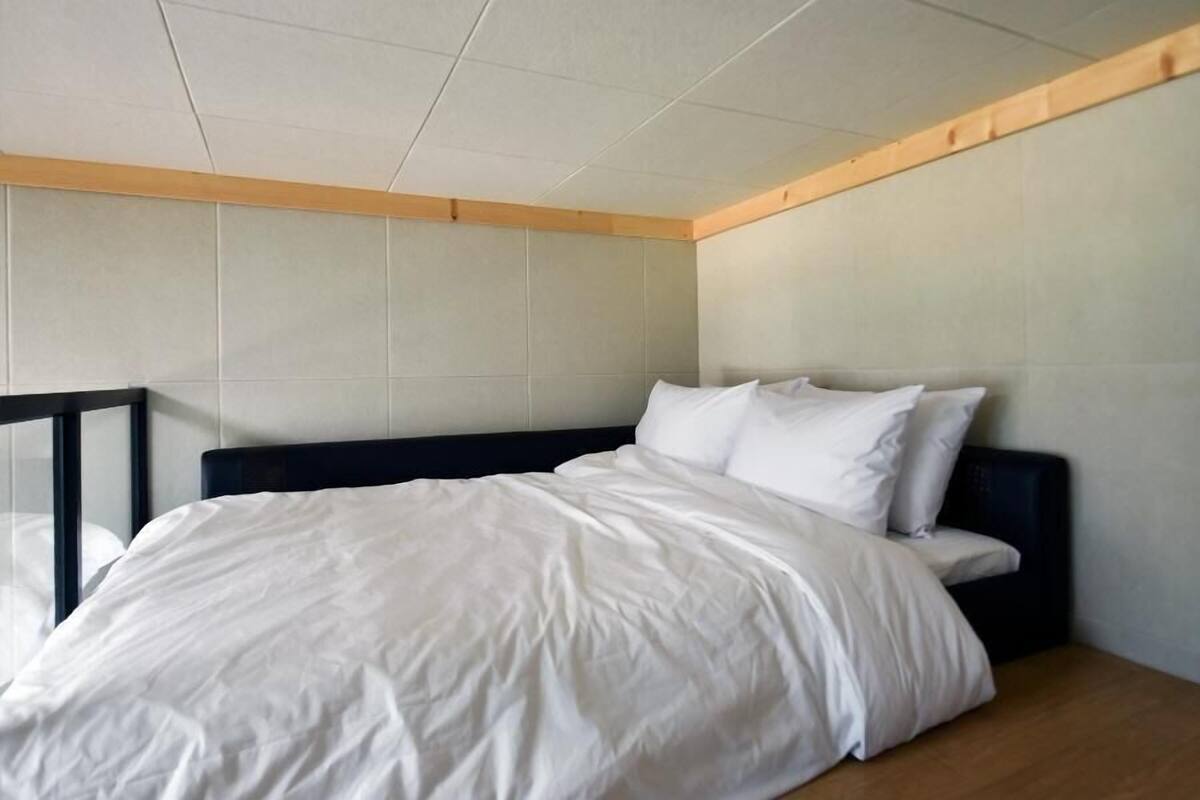Un dormitorio con cama, cabecera, viga de techo de madera y paredes blancas.