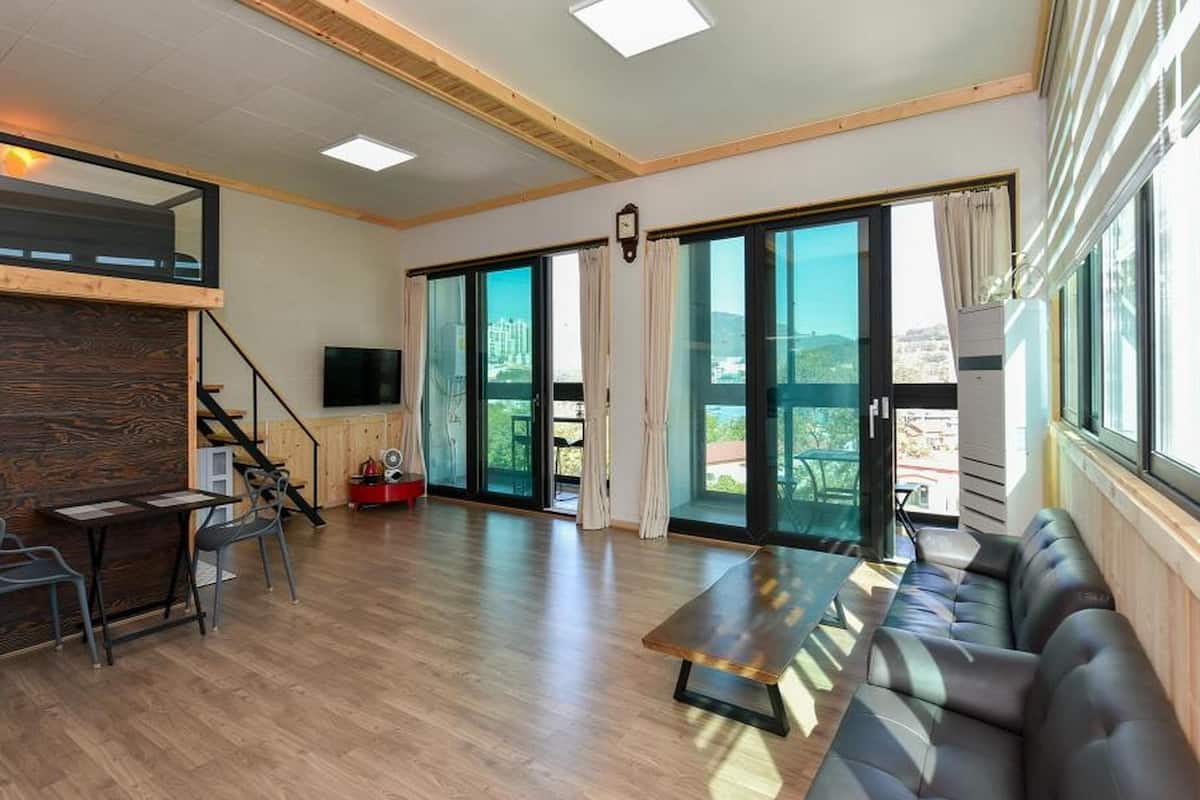 Amplia sala de estar con piso de madera, un sofá, una mesa de comedor y un televisor. Amplias puertas correderas de vidrio dan acceso a un balcón.