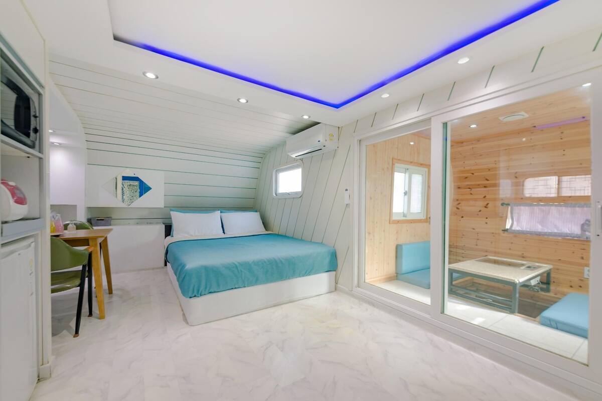 A modern bedroom with a bed, a desk, and a sliding glass door leading to a wooden deck.