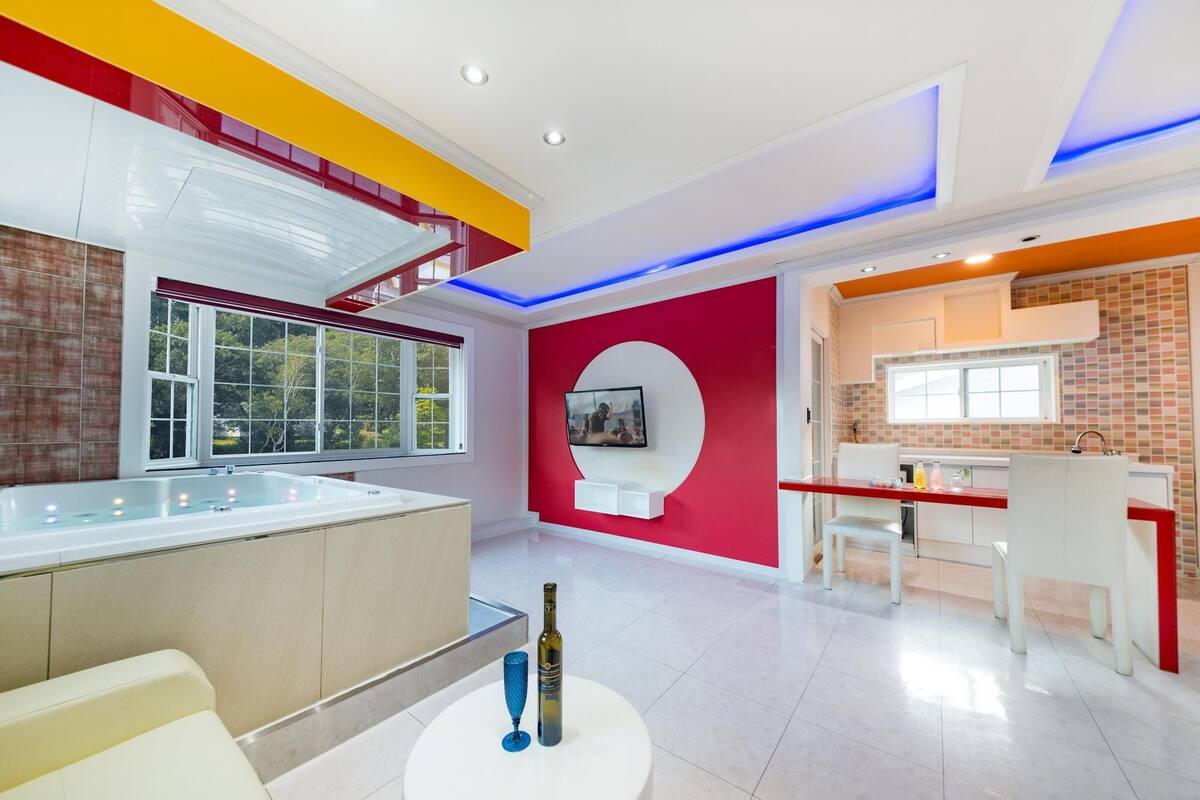 A modern kitchen with a red accent wall, a white dining area, and a large window.