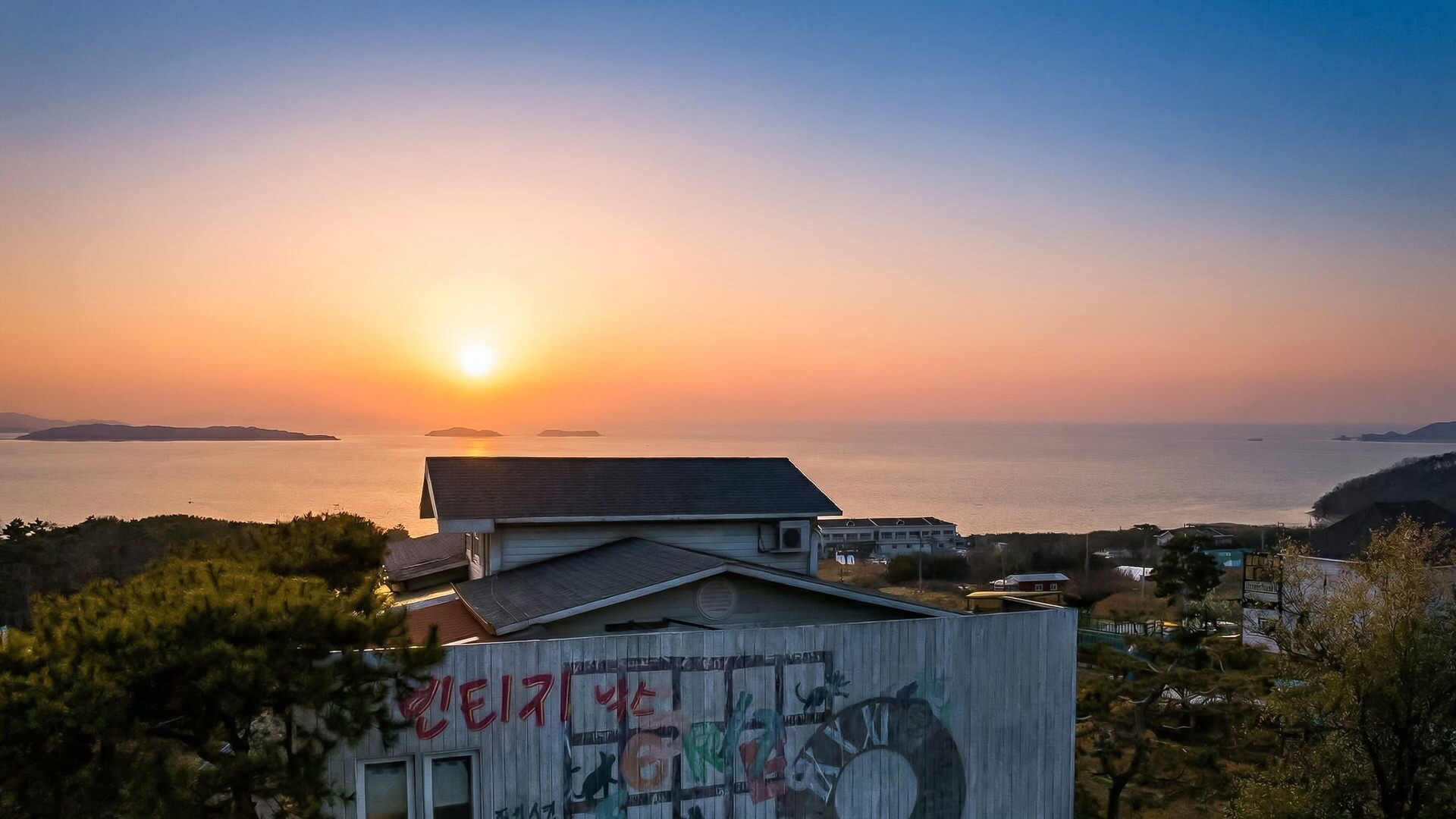 A coastal view with a sunset, a building with graffiti, and a clear sky.