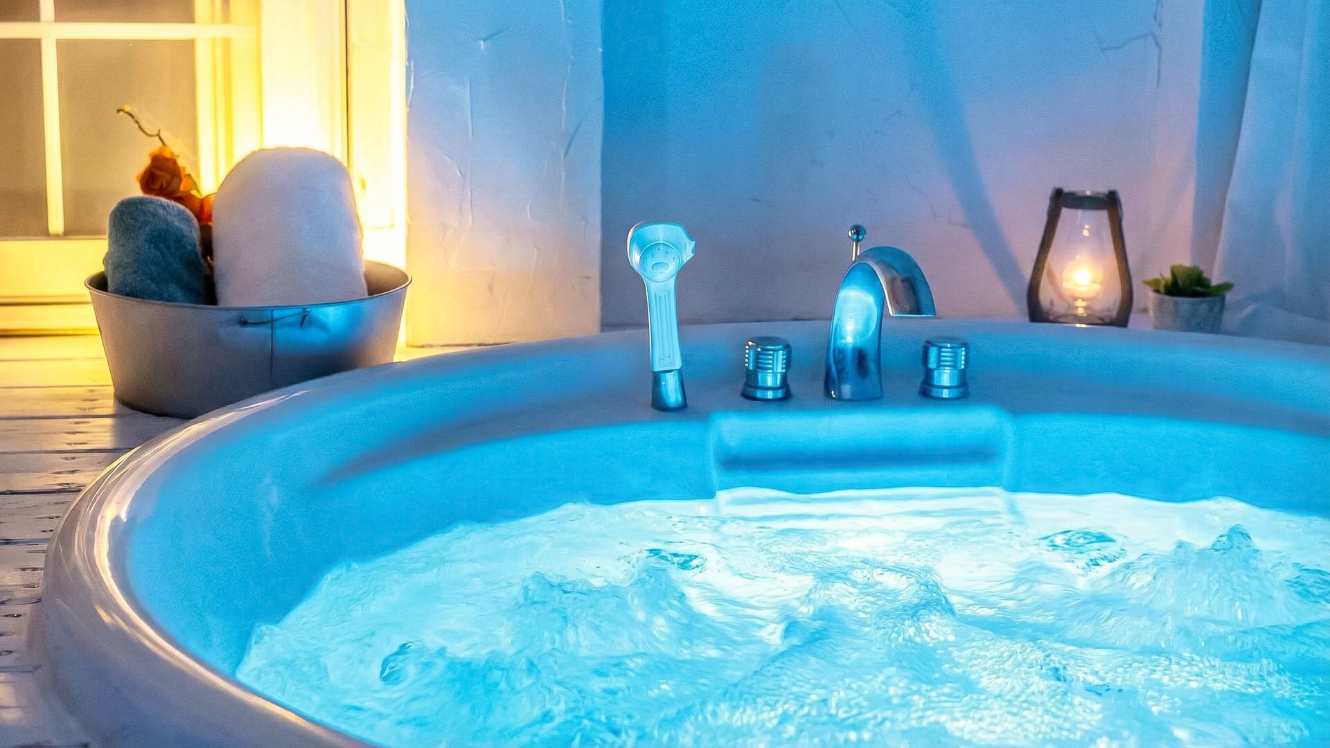 A hot tub with a faucet and controls, a bucket with stones, and a candle on a table.