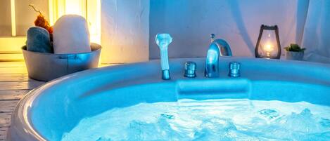 A hot tub with a faucet and controls, a bucket with stones, and a candle on a table.