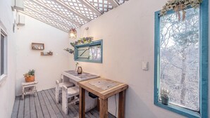 A cozy outdoor seating area with a wooden table and chairs, a small stool, and a window with a view of trees. - Ganghwa Vintage Box Pension (Incheon)