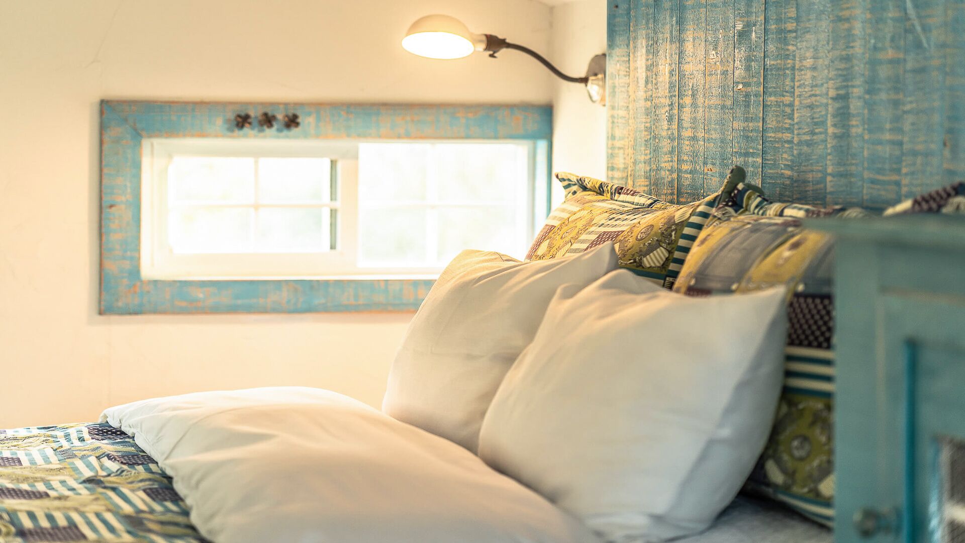 A bed with patterned bedding, a window with a view, and a wall with a decorative element.