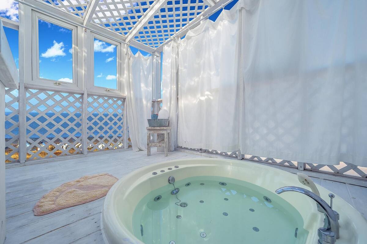 Un bain à remous avec vue sur la mer, une terrasse en bois et un espace couvert doté d’une structure en treillis.