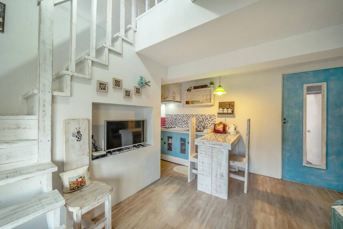 Une cuisine avec des meubles blancs, une porte bleue et un escalier en bois.