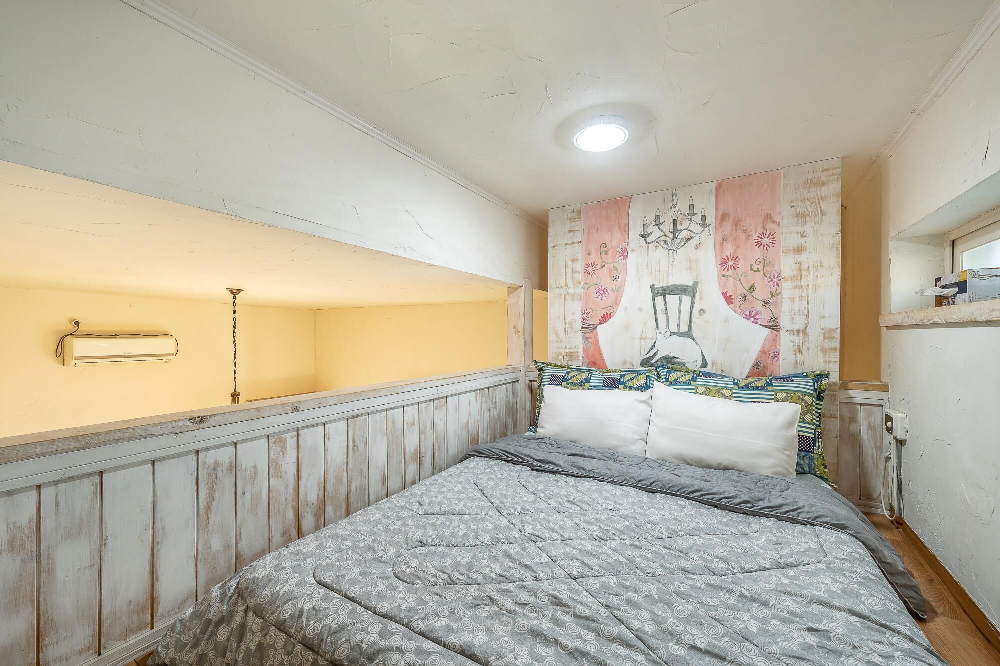 Une chambre à coucher comprenant un lit, un ventilateur de plafond, un radiateur fixé au mur et une tapisserie décorative.