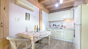 Une cuisine avec des meubles blancs, une table à manger recouverte d’une nappe à motifs floraux, des chaises en osier et un réfrigérateur.