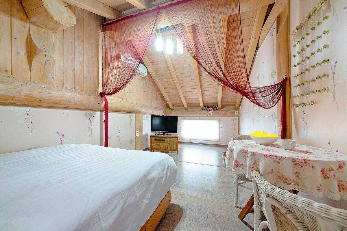 A bedroom with a bed, a television, a table with a bowl, and a window.