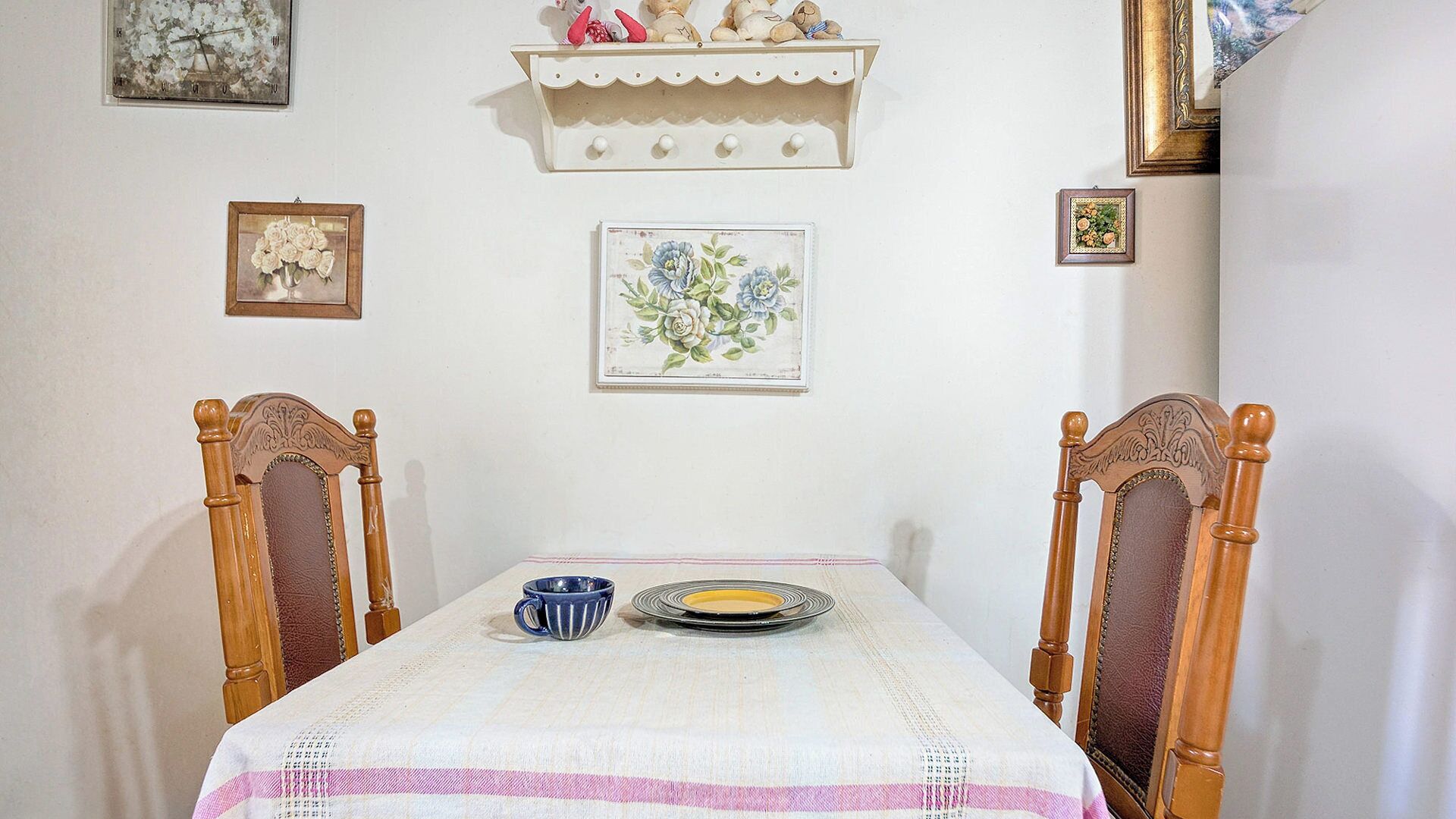 A dining table with a white tablecloth and a blue cup, flanked by wooden chairs with carved details.