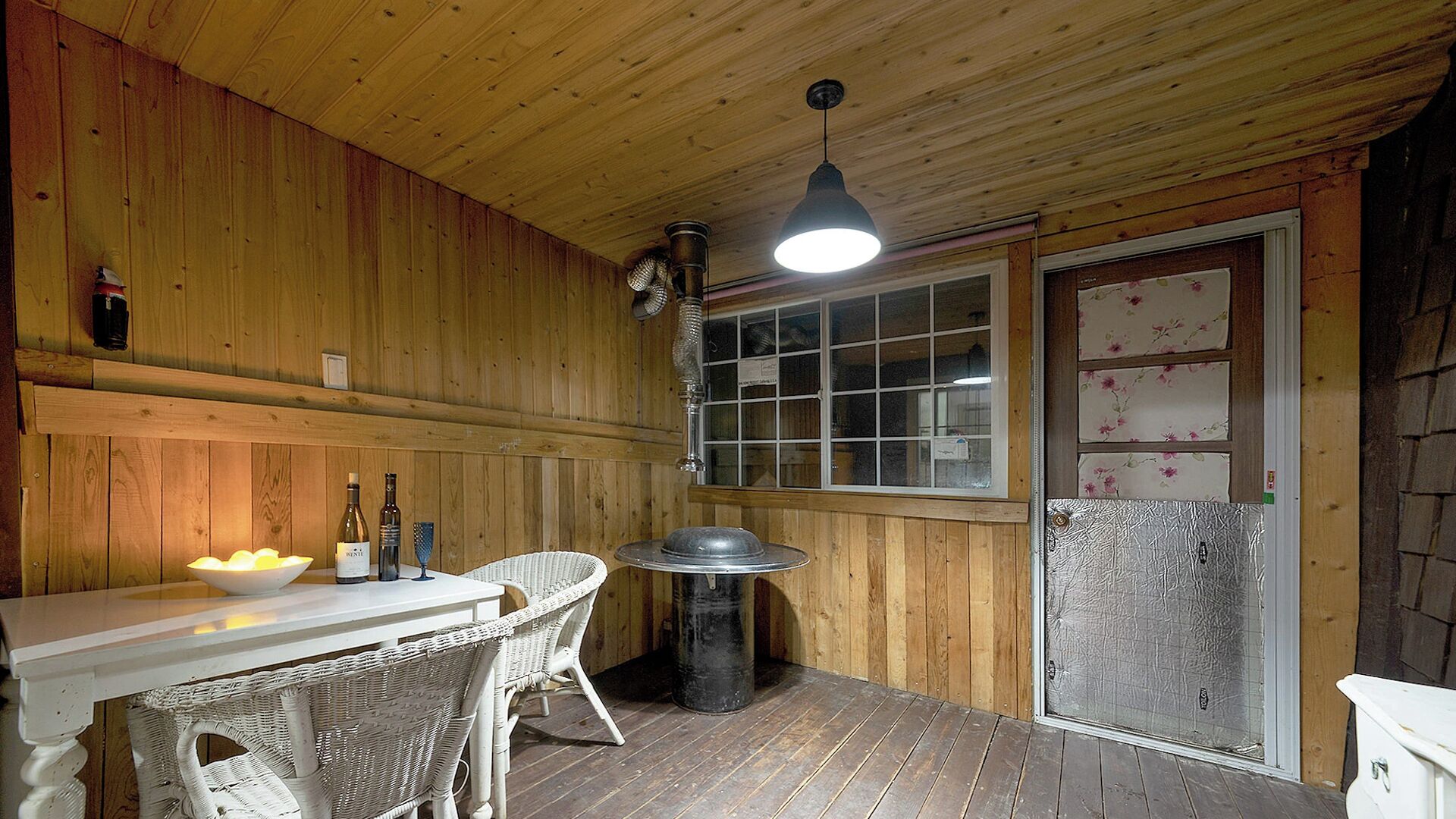 Un interior de madera con una mesa, sillas, una lámpara colgante y una ventana con vidrio esmerilado.