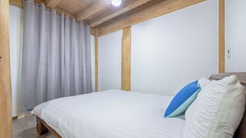 A bedroom with a wooden ceiling, a bed with white bedding and two pillows, and a window with curtains.