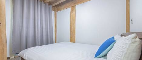 Un dormitorio con techo de madera, una cama con ropa blanca y dos almohadas, y una ventana con cortinas.