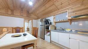 A compact kitchen with a dining area, wooden ceiling, and white cabinetry. - Ganghwa Izba Pension (Incheon)