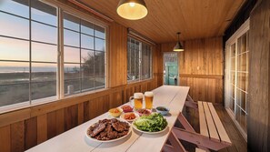 A wooden interior with a long table set for dining, large windows, and a view of the outdoors. - Ganghwa Izba Pension (Incheon)