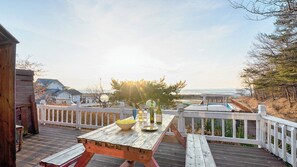 Una terraza de madera con una mesa de picnic y baranda, con vista a una playa y al océano.