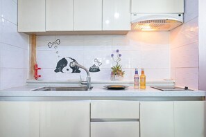 A kitchen with white cabinets, a stainless steel sink, a red faucet, and a decorative wall with a dog and bone design. - Ganghwa Izba Pension (Incheon)