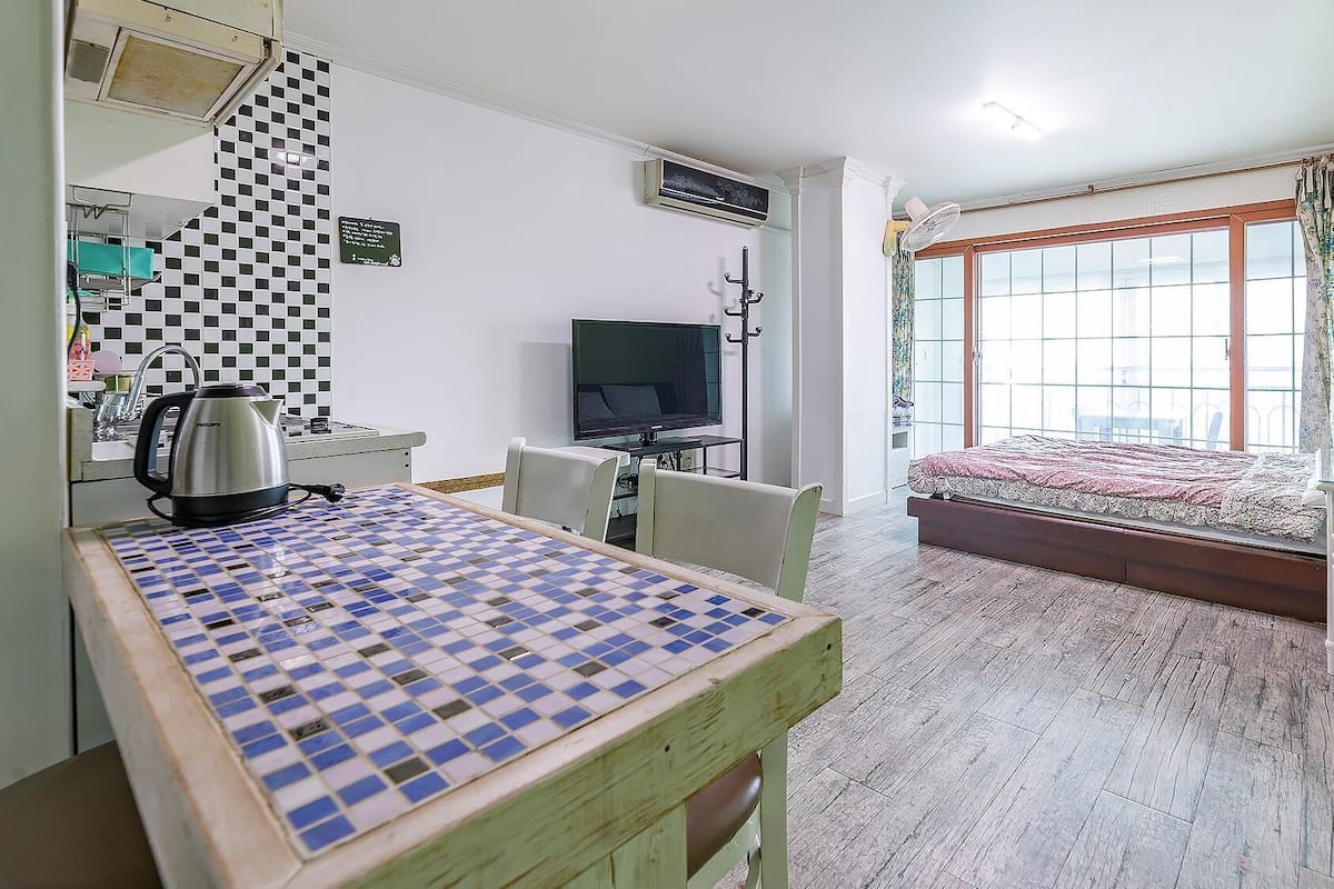 Una habitació amb una taula estampada, un llit amb colcha floral, una televisió i una finestra amb cortines.