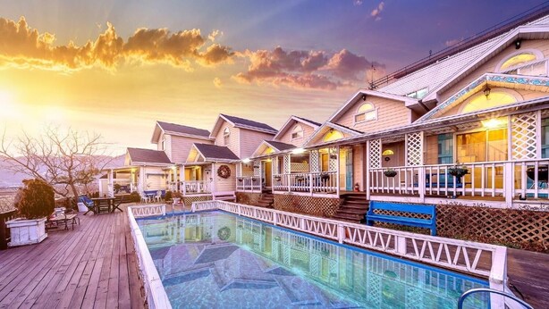 A swimming pool with a wooden deck, surrounded by buildings with balconies and a sunset in the background. - Ganghwa Edenjungwon Pension (Incheon)