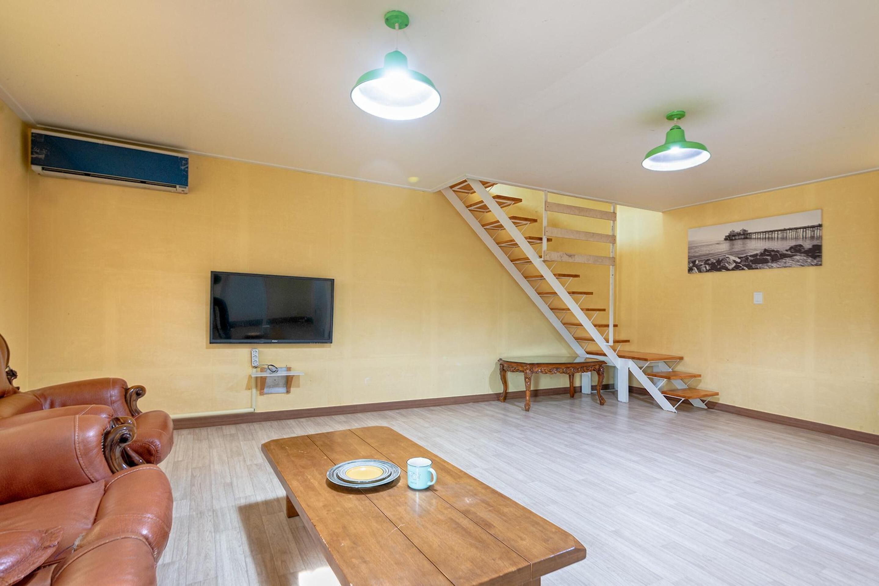 A living room with a wooden staircase, a television mounted on the wall, a leather sofa, and a wooden coffee table.