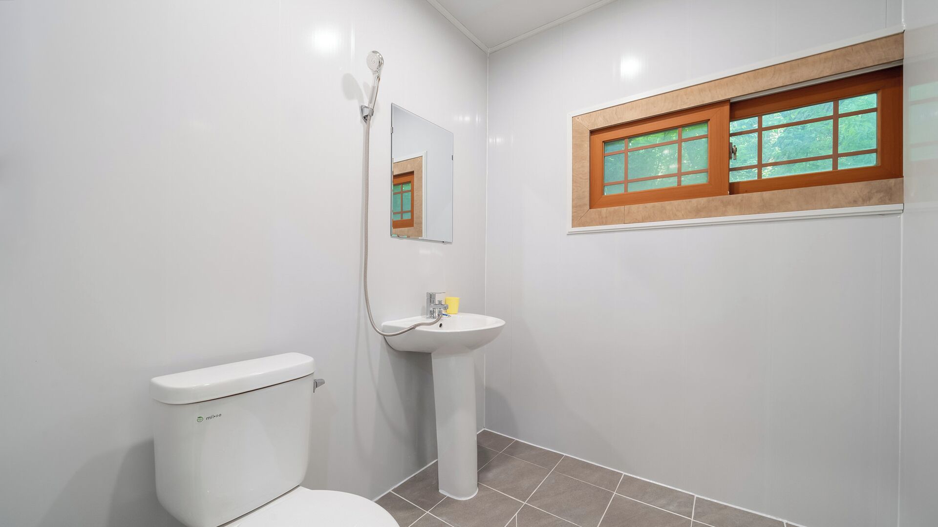 A bathroom with a toilet, sink, shower, and a window with a wooden frame.