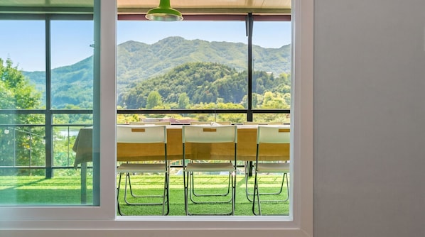 A room with a large window overlooking a mountainous landscape, a table with chairs, and a hanging light fixture.