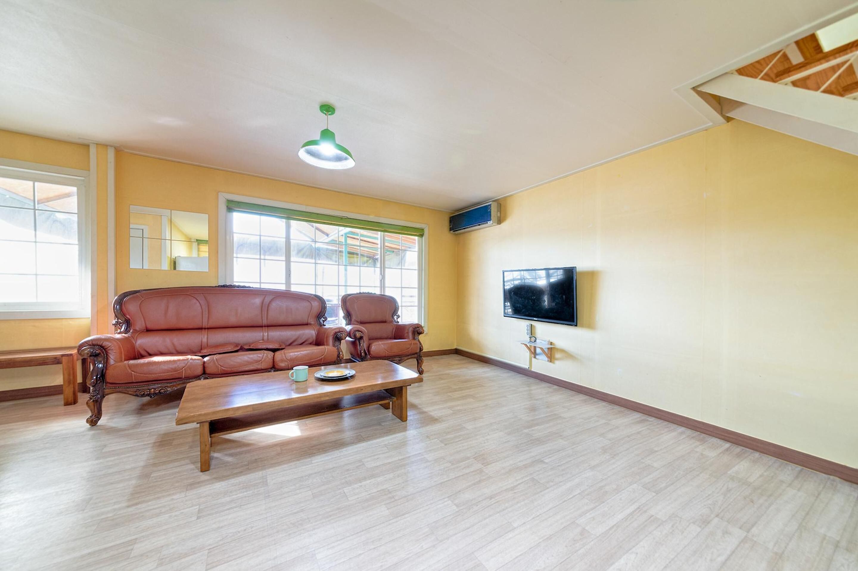 A living room with a brown leather sofa, a wooden coffee table, and a flat-screen TV mounted on the wall.