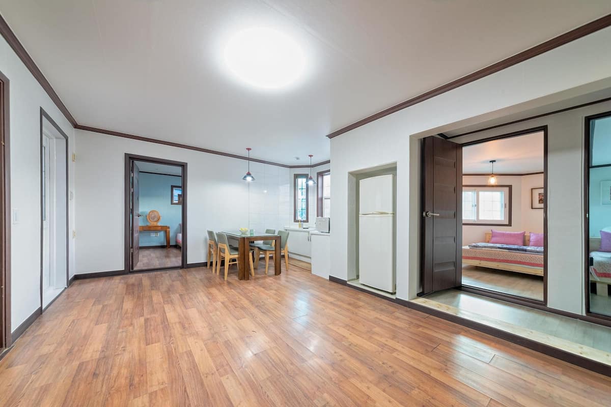 Une pièce spacieuse avec un plancher en bois, un coin repas comprenant une table et des chaises, et un lit visible à travers une porte ouverte.