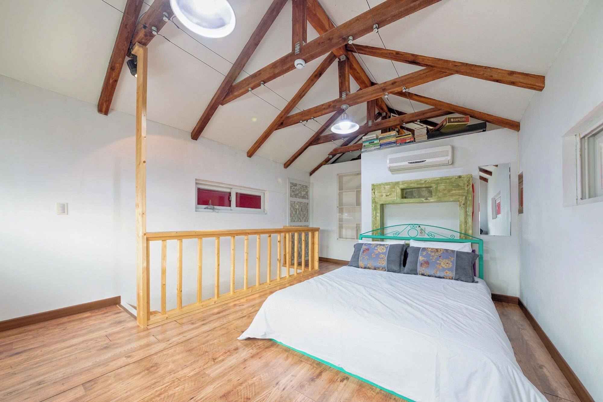 Un dormitorio con techo de madera, una cama con colchón blanco, cabecera de metal verde y baranda de madera.
