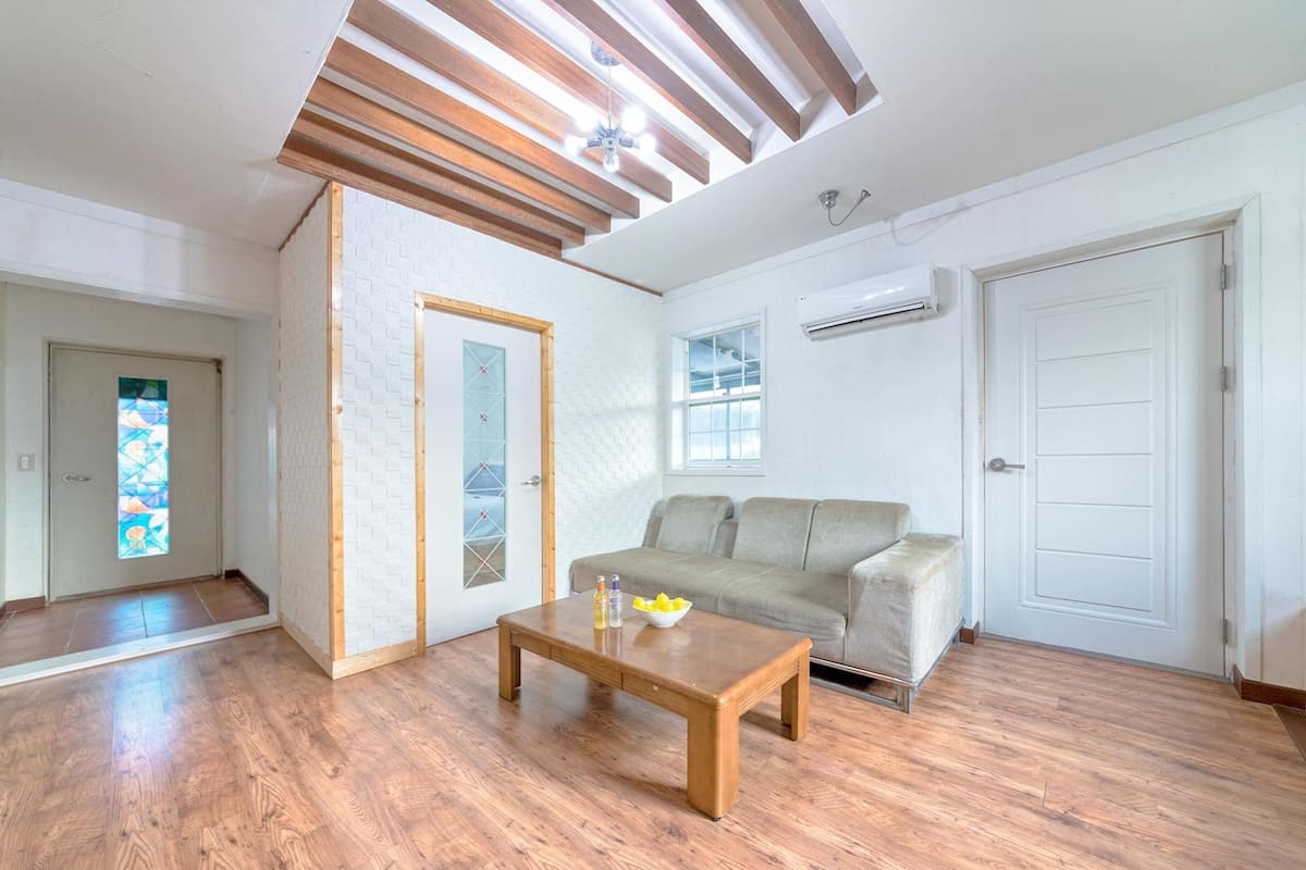 Un salon avec un plancher en bois, un canapé beige, une table basse en bois et une porte blanche.
