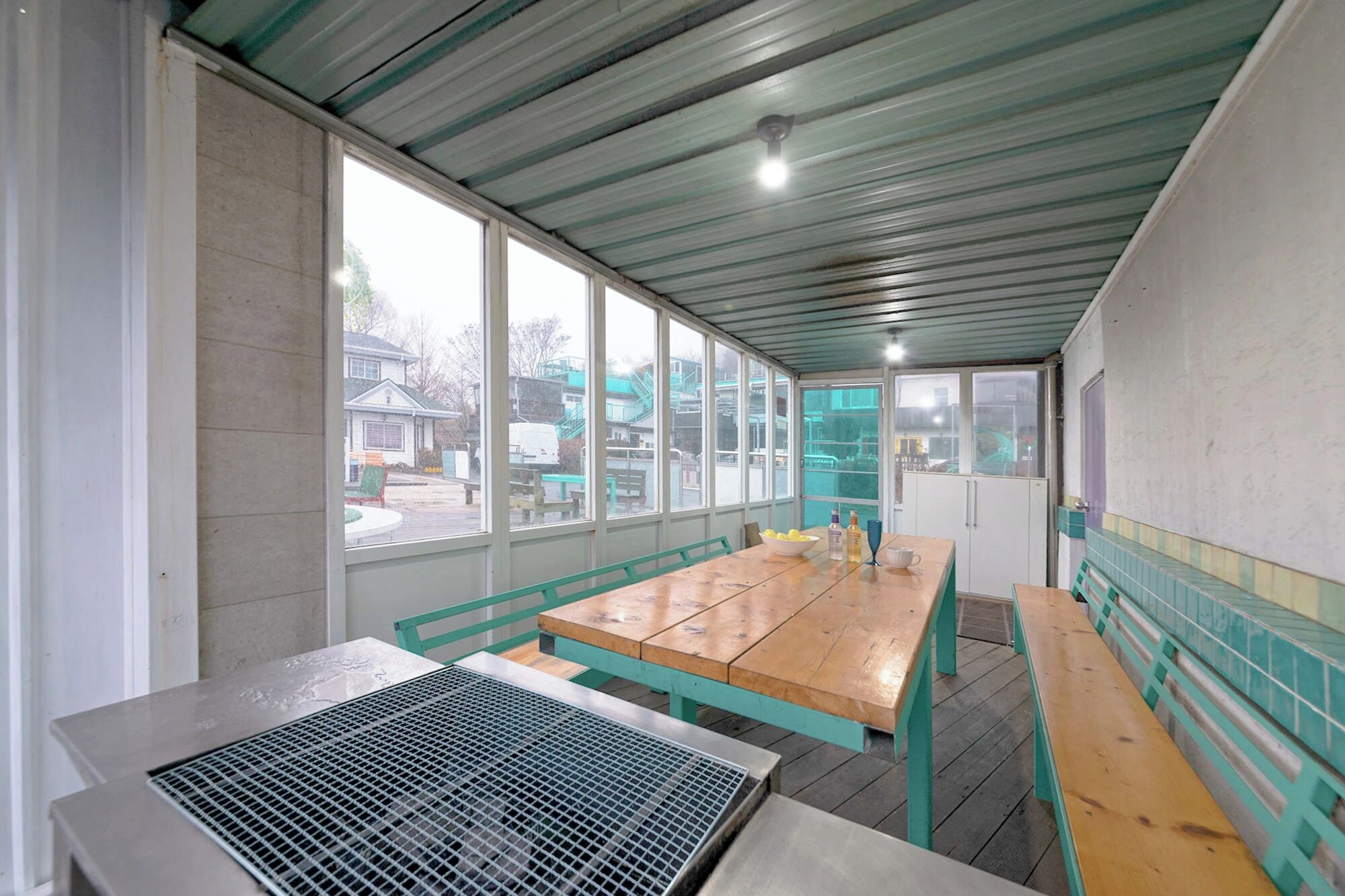 Un espace extérieur abrité, doté de tables et de bancs, de grandes fenêtres et d’un plafond en métal.