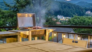 A barbecue grill with food on a balcony overlooking a mountainous area. - Gapyeong Four Season Pension (Gapyeong)