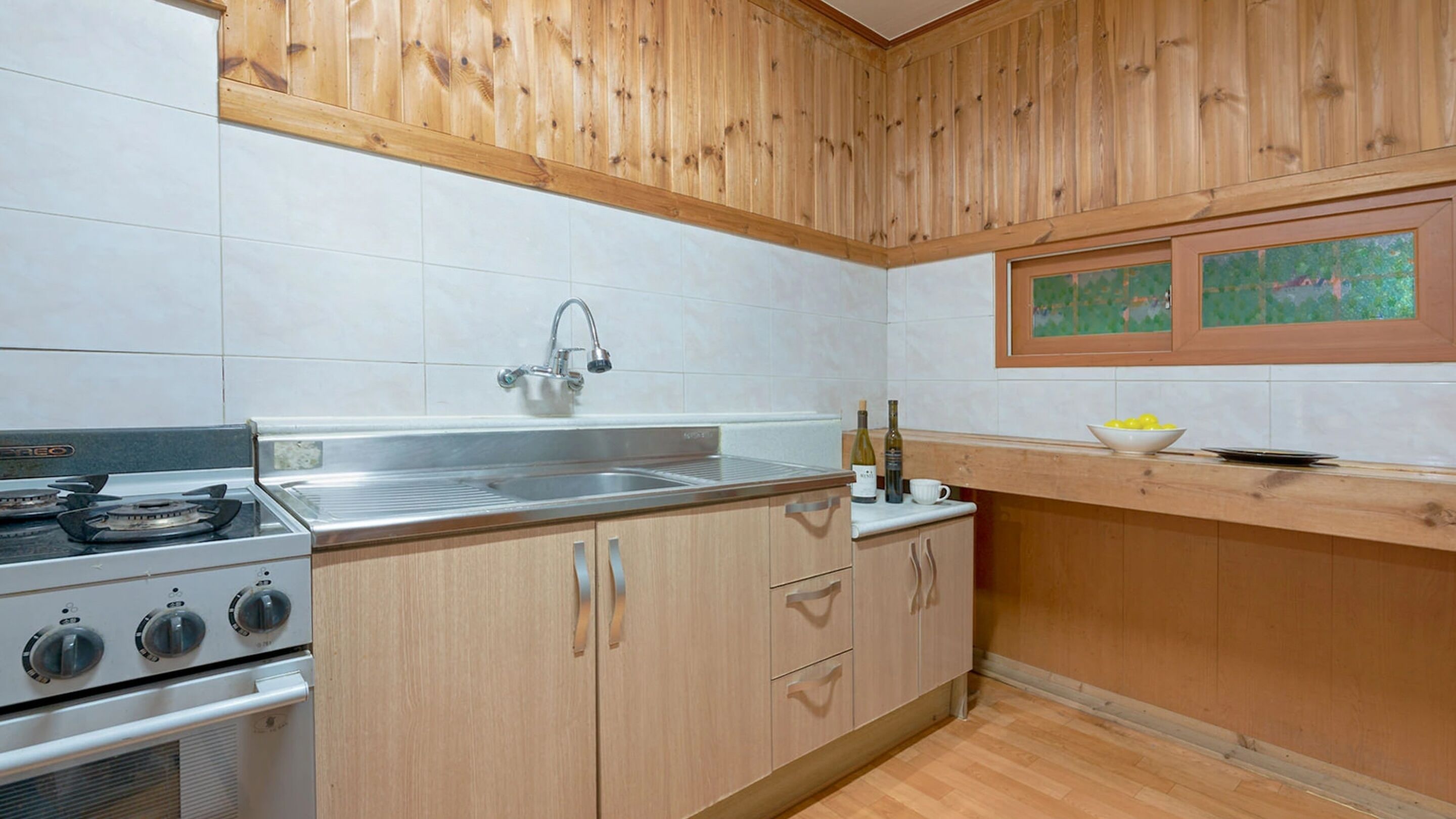 Una cocina con armarios de madera, un lavamanos de acero inoxidable, una estufa y una ventana con un cuadro.