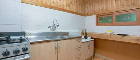 Una cocina con armarios de madera, un lavamanos de acero inoxidable, una estufa y una ventana con un cuadro.