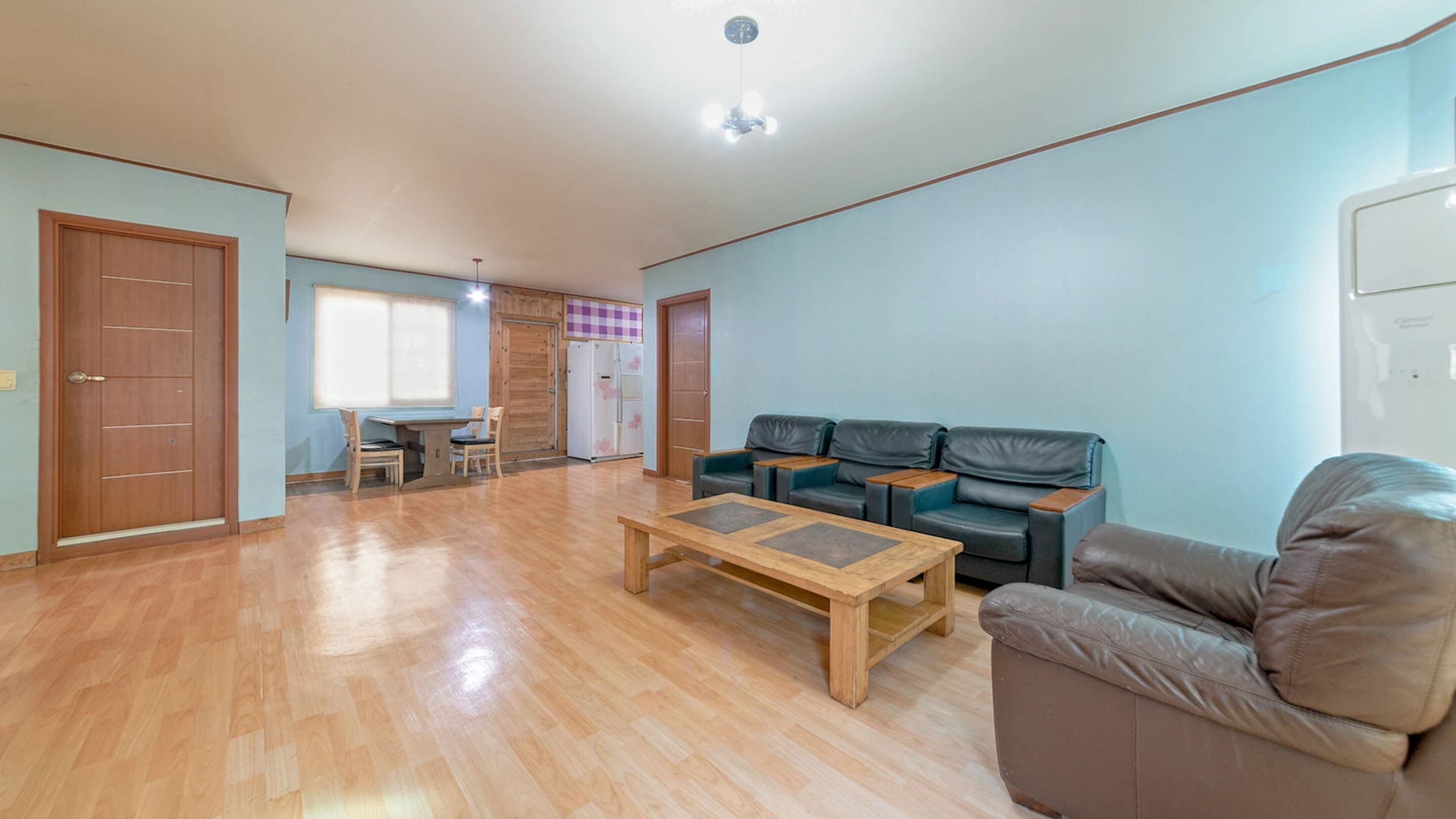 A spacious living room with a wooden coffee table, a sofa, and a dining area with a table and chairs.